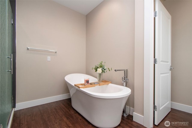 bathroom with a freestanding tub, baseboards, and wood finished floors