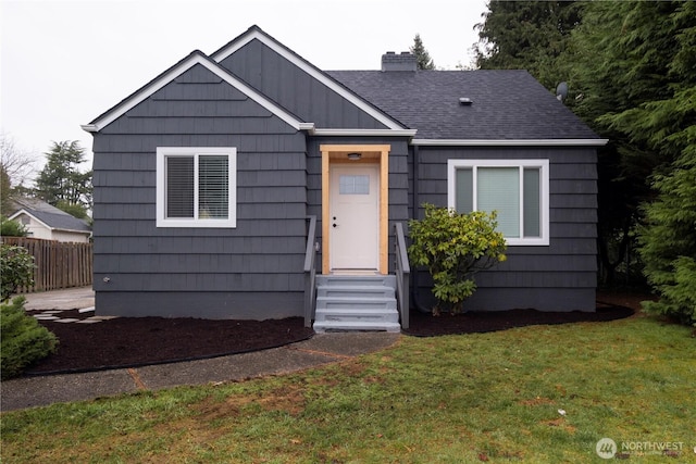 view of front facade featuring a front lawn, fence, entry steps, roof with shingles, and a chimney