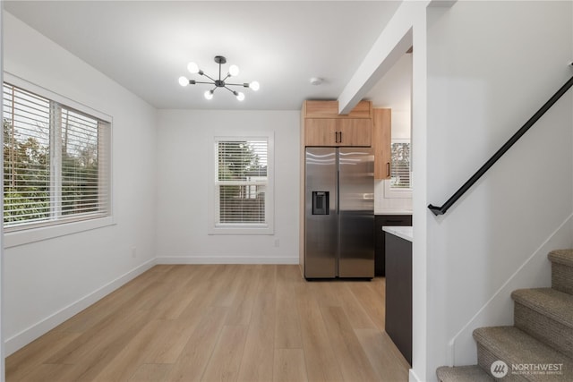 kitchen featuring an inviting chandelier, light wood-style flooring, stainless steel fridge with ice dispenser, and baseboards