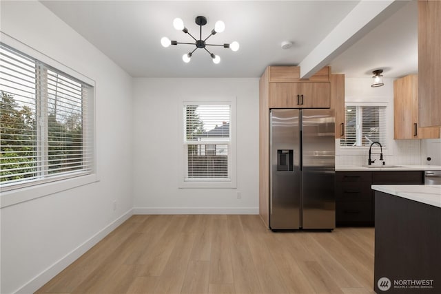 kitchen featuring light wood finished floors, baseboards, light countertops, appliances with stainless steel finishes, and a sink