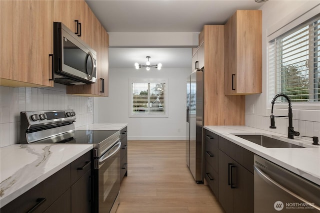 kitchen featuring light wood-style flooring, a sink, light stone counters, tasteful backsplash, and appliances with stainless steel finishes