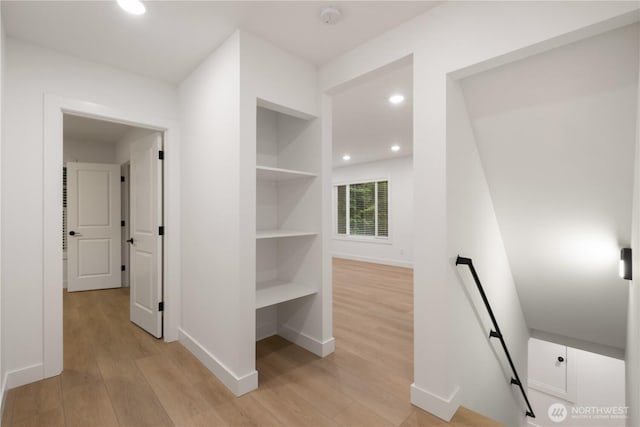 corridor featuring light wood finished floors, visible vents, built in shelves, baseboards, and an upstairs landing