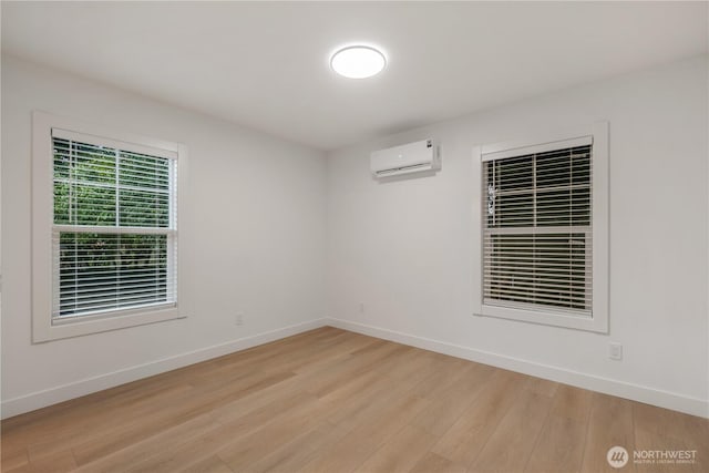 spare room with light wood-style floors, a wall mounted AC, and baseboards