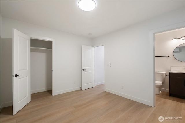 unfurnished bedroom with ensuite bath, a closet, baseboards, and light wood finished floors