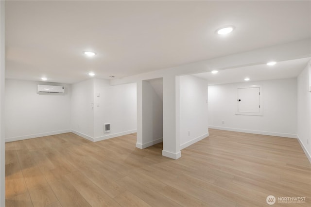 finished below grade area featuring recessed lighting, visible vents, light wood finished floors, and a wall mounted AC