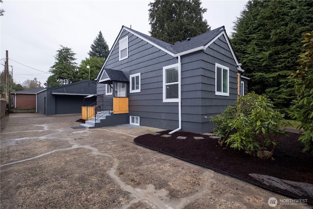 exterior space featuring a garage, roof with shingles, and an outdoor structure