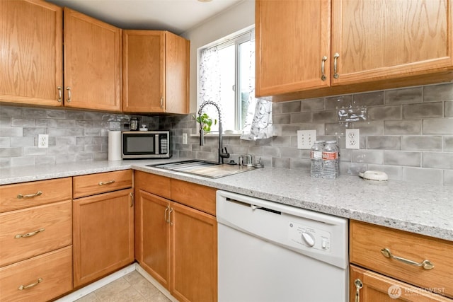 kitchen with light tile patterned floors, stainless steel microwave, decorative backsplash, white dishwasher, and a sink