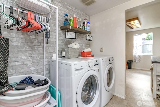 clothes washing area featuring laundry area, brick wall, visible vents, and separate washer and dryer