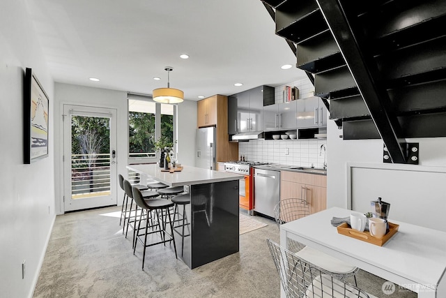 kitchen with tasteful backsplash, appliances with stainless steel finishes, a sink, modern cabinets, and a kitchen bar