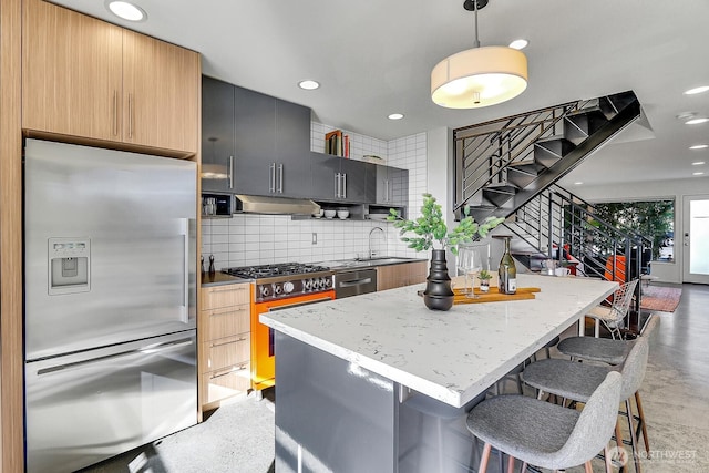 kitchen with decorative backsplash, appliances with stainless steel finishes, a breakfast bar, under cabinet range hood, and a sink