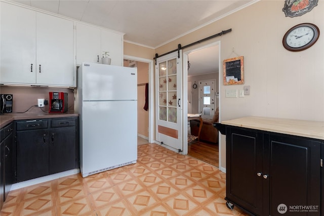 kitchen featuring a barn door, ornamental molding, freestanding refrigerator, white cabinets, and dark cabinetry