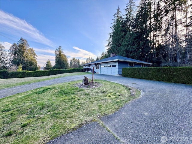 view of front of home featuring driveway, an attached garage, a chimney, and a front lawn