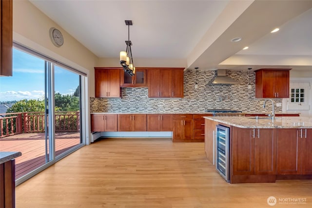 kitchen with decorative backsplash, wine cooler, wall chimney exhaust hood, and light wood-style flooring