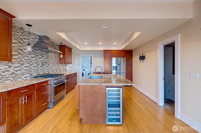 kitchen featuring wall chimney range hood, wine cooler, washer and clothes dryer, stainless steel appliances, and a sink