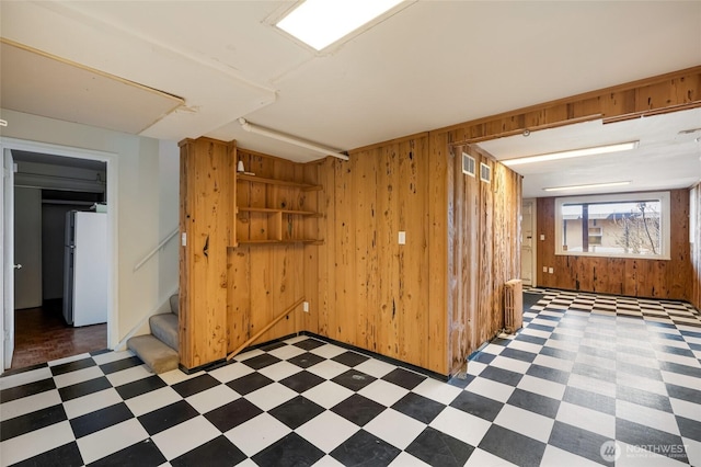 basement with stairway, wooden walls, light floors, and freestanding refrigerator