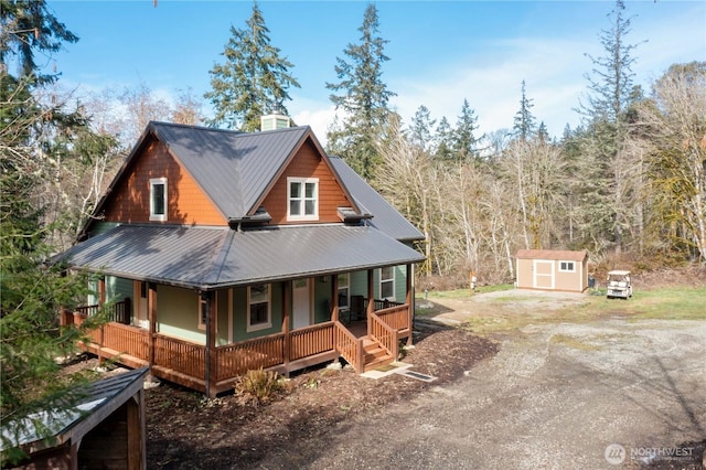 view of front of home with dirt driveway, metal roof, a storage unit, an outdoor structure, and a porch