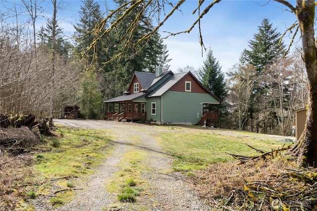 view of side of property featuring metal roof, driveway, a yard, and a chimney