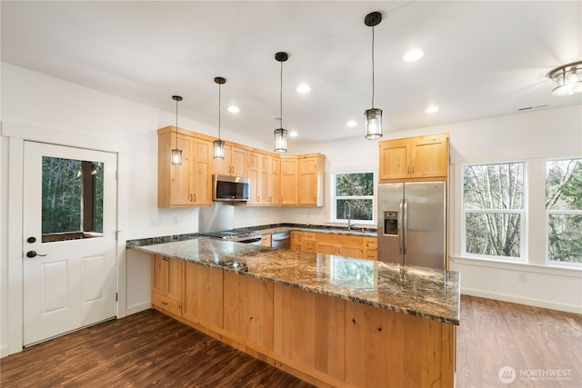 kitchen featuring stainless steel appliances, a peninsula, a sink, dark stone counters, and light brown cabinetry