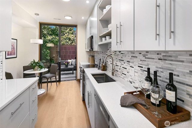 kitchen featuring a sink, light countertops, appliances with stainless steel finishes, open shelves, and tasteful backsplash