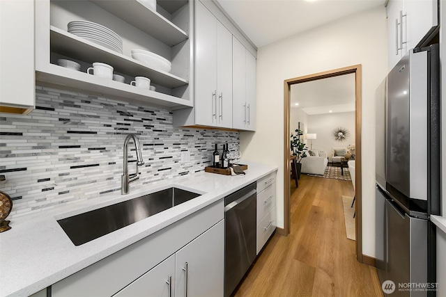 kitchen with white cabinets, stainless steel appliances, light wood-type flooring, open shelves, and a sink