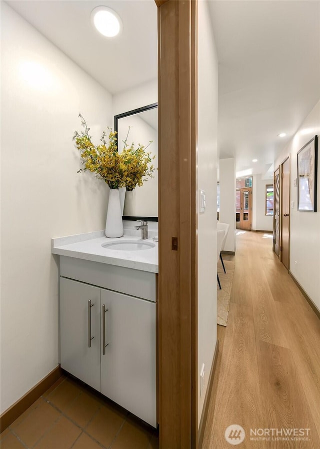 hallway with baseboards, recessed lighting, a sink, and light wood-style floors