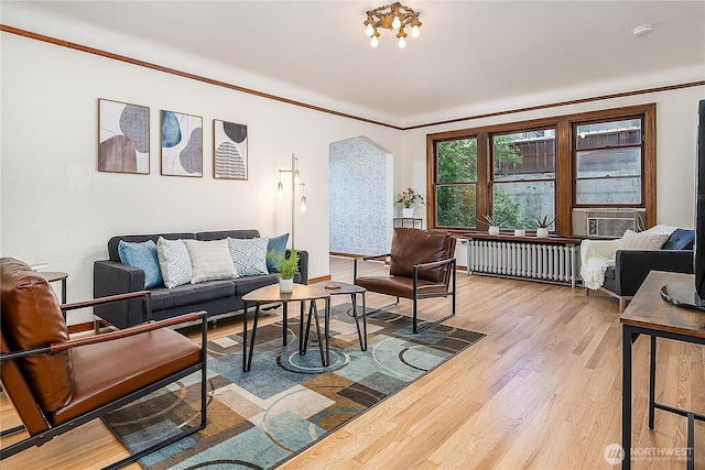 living area featuring arched walkways, radiator heating unit, light wood-style floors, ornamental molding, and cooling unit