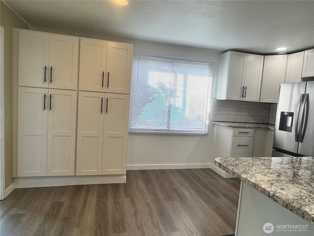 kitchen with stainless steel fridge, decorative backsplash, white cabinets, dark wood-style flooring, and light stone countertops