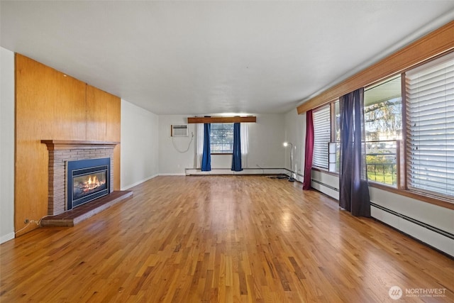 unfurnished living room featuring a wall unit AC, a fireplace, a baseboard radiator, light wood-style flooring, and a baseboard heating unit