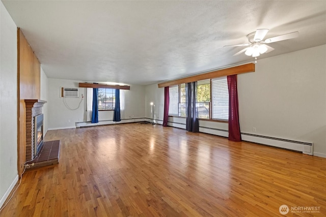 unfurnished living room featuring a ceiling fan, a brick fireplace, wood finished floors, a wall mounted air conditioner, and baseboards