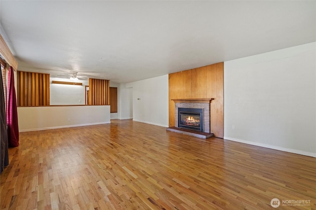 unfurnished living room with light wood-style floors, a fireplace, baseboards, and a ceiling fan