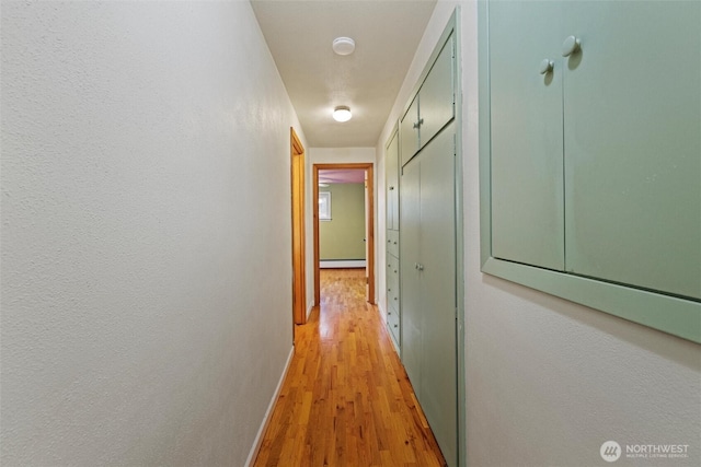 corridor with light wood-type flooring, baseboards, and baseboard heating