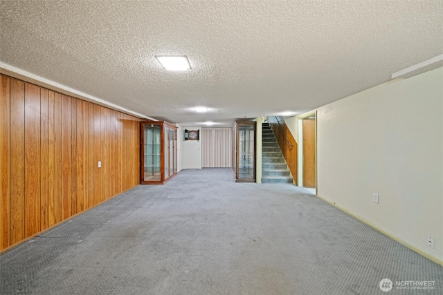 finished basement with a textured ceiling, carpet floors, wood walls, and stairway