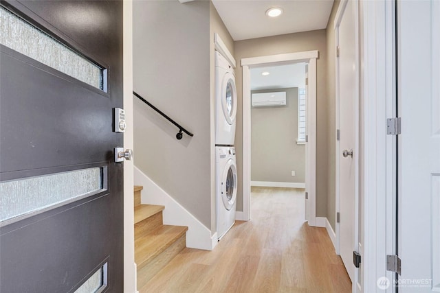 entrance foyer featuring stacked washer and dryer, light wood-style floors, an AC wall unit, baseboards, and stairs