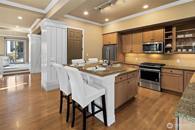 kitchen featuring dark stone counters, appliances with stainless steel finishes, wood finished floors, a breakfast bar area, and backsplash