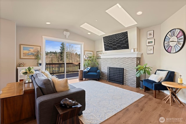 living room with lofted ceiling with skylight, recessed lighting, a fireplace, and wood finished floors