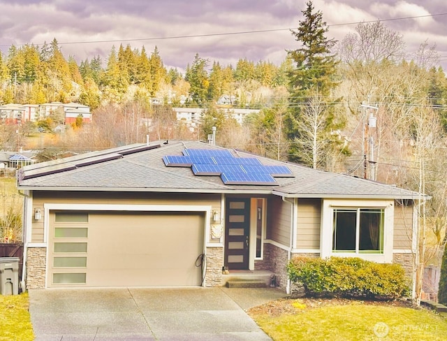 prairie-style house with a garage, solar panels, stone siding, concrete driveway, and roof with shingles