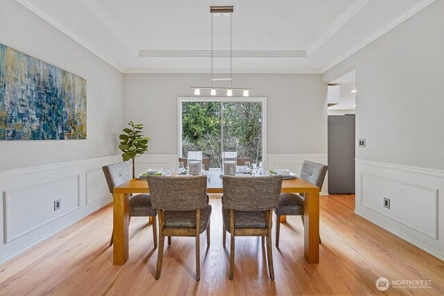 dining area featuring light wood-type flooring, a tray ceiling, and ornamental molding