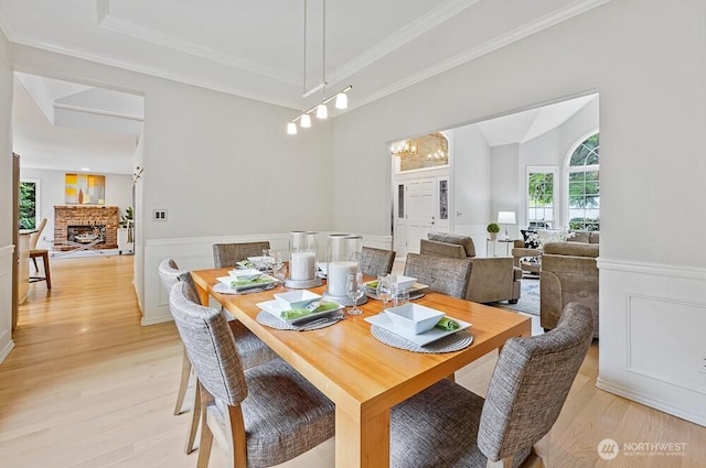 dining area with crown molding, a brick fireplace, wainscoting, and light wood finished floors