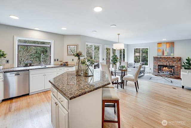 kitchen with dishwasher, light wood-style flooring, a kitchen breakfast bar, plenty of natural light, and a sink