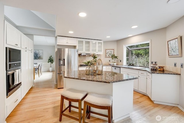 kitchen with dark stone countertops, light wood finished floors, a sink, appliances with stainless steel finishes, and white cabinetry