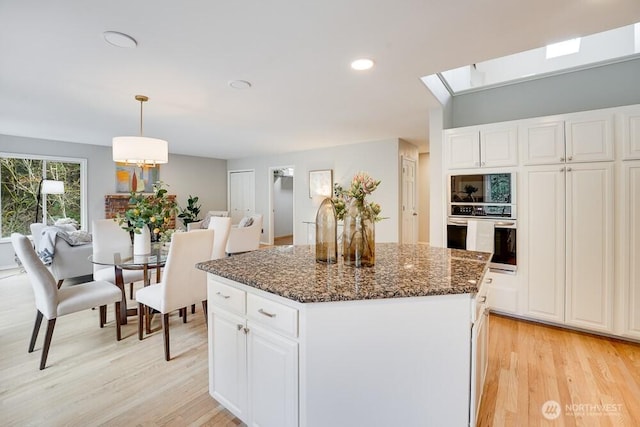 kitchen with light wood-style flooring, a center island, dark stone counters, white cabinets, and stainless steel oven