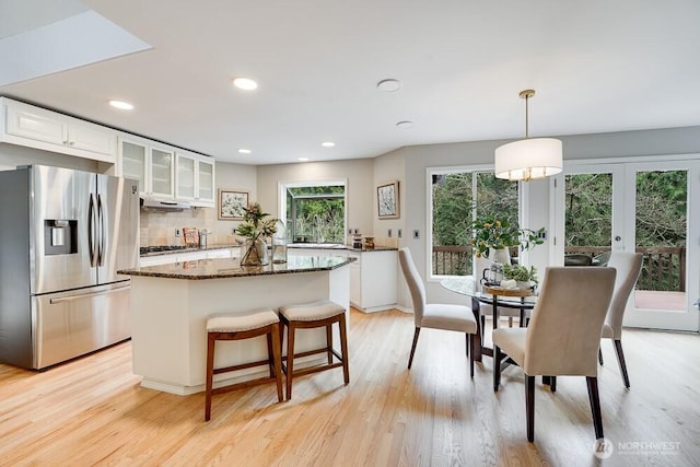 kitchen featuring white cabinets, light wood-style floors, glass insert cabinets, stainless steel fridge, and a center island