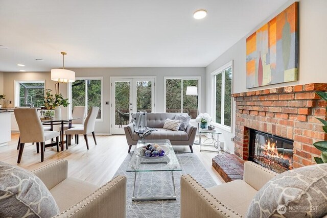 living area with a wealth of natural light, french doors, a fireplace, and light wood-style floors