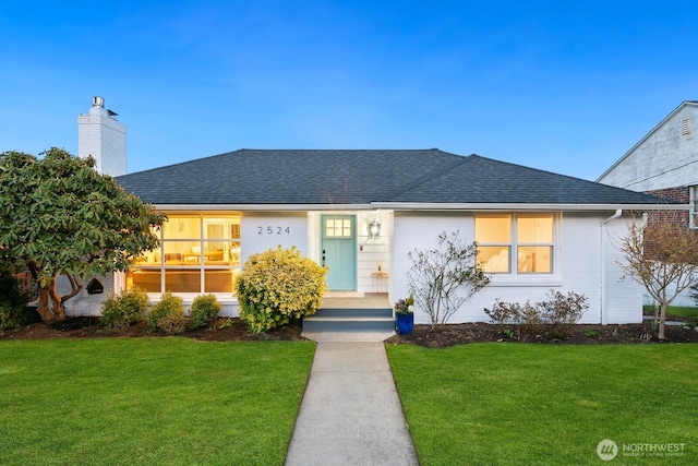 ranch-style house with a shingled roof, a chimney, and a front yard