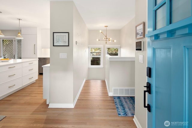 entrance foyer featuring light wood finished floors, baseboards, visible vents, and a notable chandelier