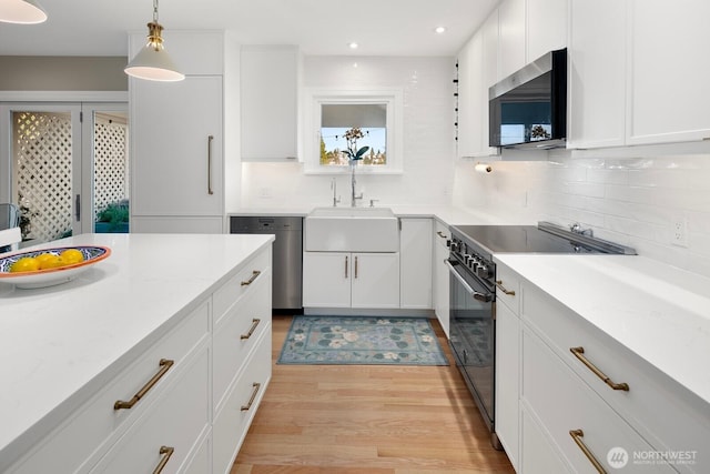 kitchen with light wood-style flooring, appliances with stainless steel finishes, backsplash, white cabinetry, and a sink