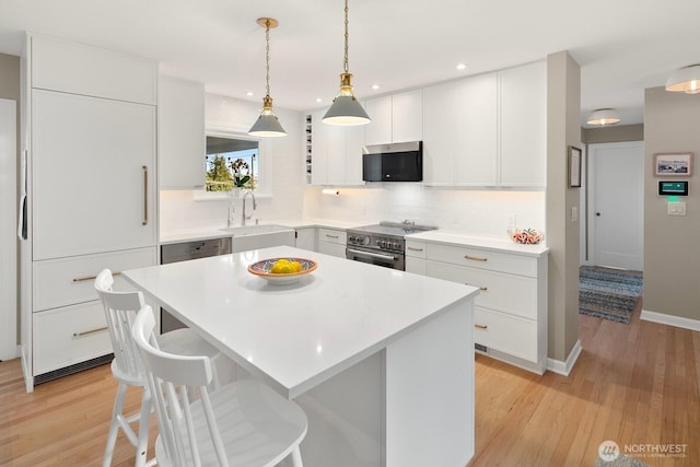 kitchen featuring a kitchen island, appliances with stainless steel finishes, a breakfast bar area, light countertops, and a sink