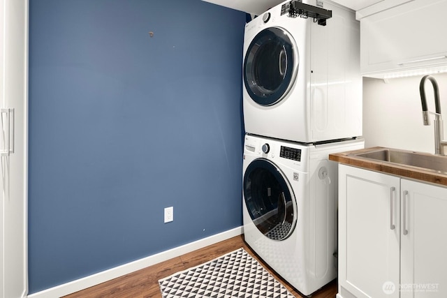 laundry room with cabinet space, baseboards, stacked washer / dryer, wood finished floors, and a sink