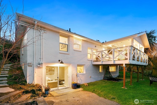 back of property featuring a wooden deck, a lawn, and brick siding