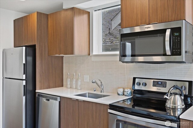 kitchen featuring brown cabinets, a sink, tasteful backsplash, appliances with stainless steel finishes, and light countertops
